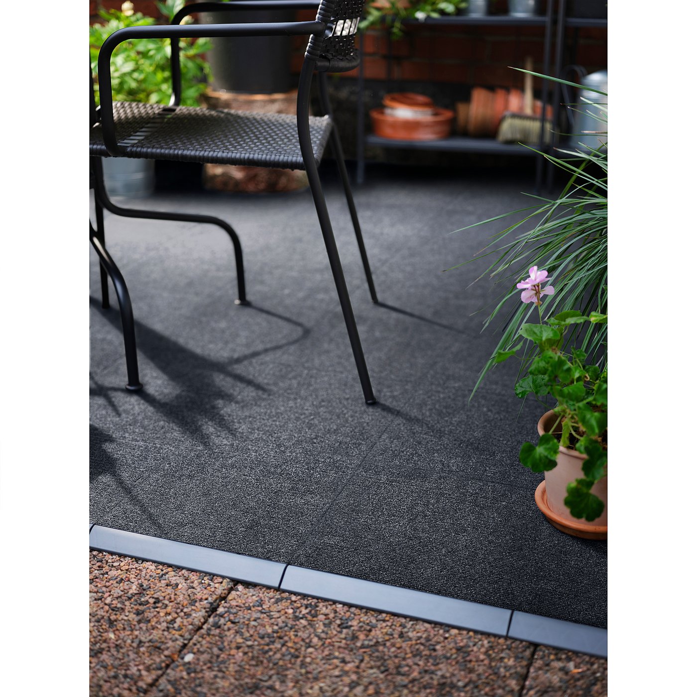 Indoor black recycled polyester RUNNEN floor decking with pink flowers in pots and metal furniture.
