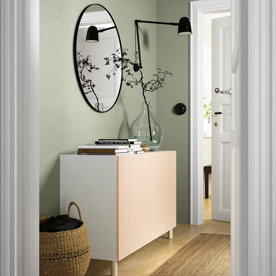 White birch cabinet in hallway, sage green wall, mirror, lamp, books, vase, basket.