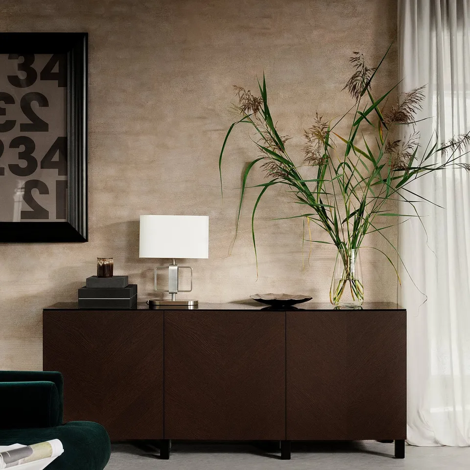 Brown wooden cabinet with white lamp and tall plant in living room.