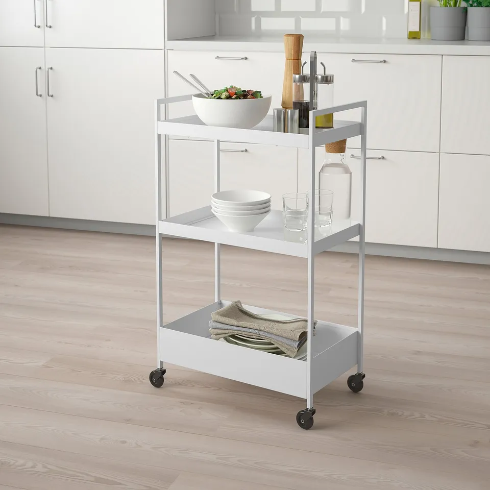 NISSAFORS white kitchen trolley with 3 shelves. Holds bowls, glasses, and folded towels. Fits small spaces, mobile on castors.