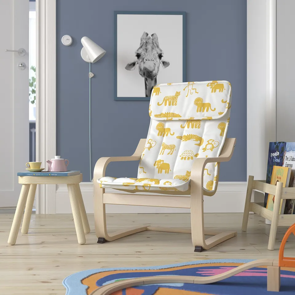 Kids corner with POÄNG chair & animal print cushion, colourful rug, small table, giraffe poster, blue wall.
