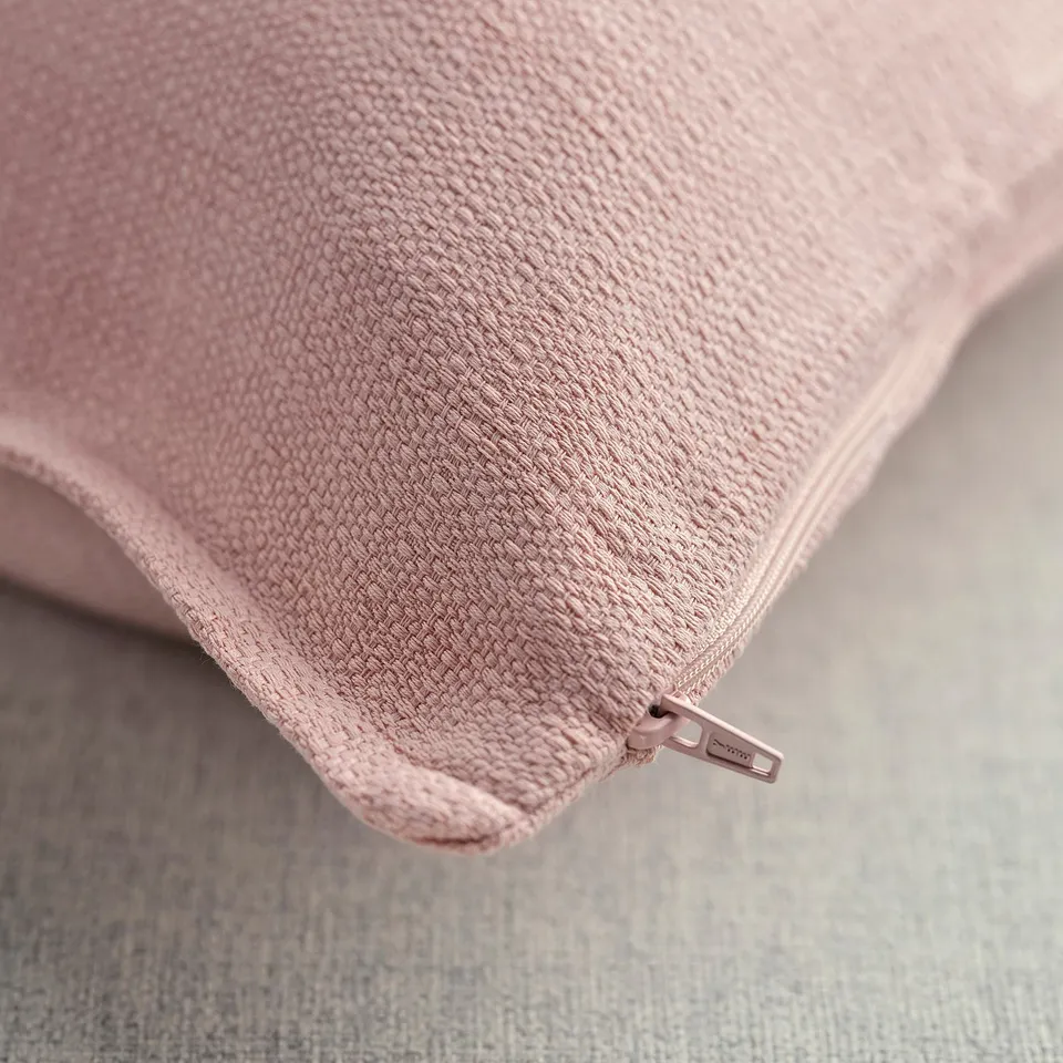 Light pink cushion cover with textured surface, zip detail, placed on a light grey fabric.