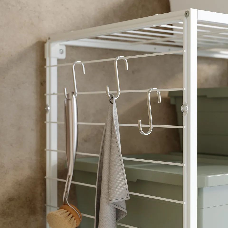 A white JOSTEIN storage grid with hooks hanging towels and a brush.