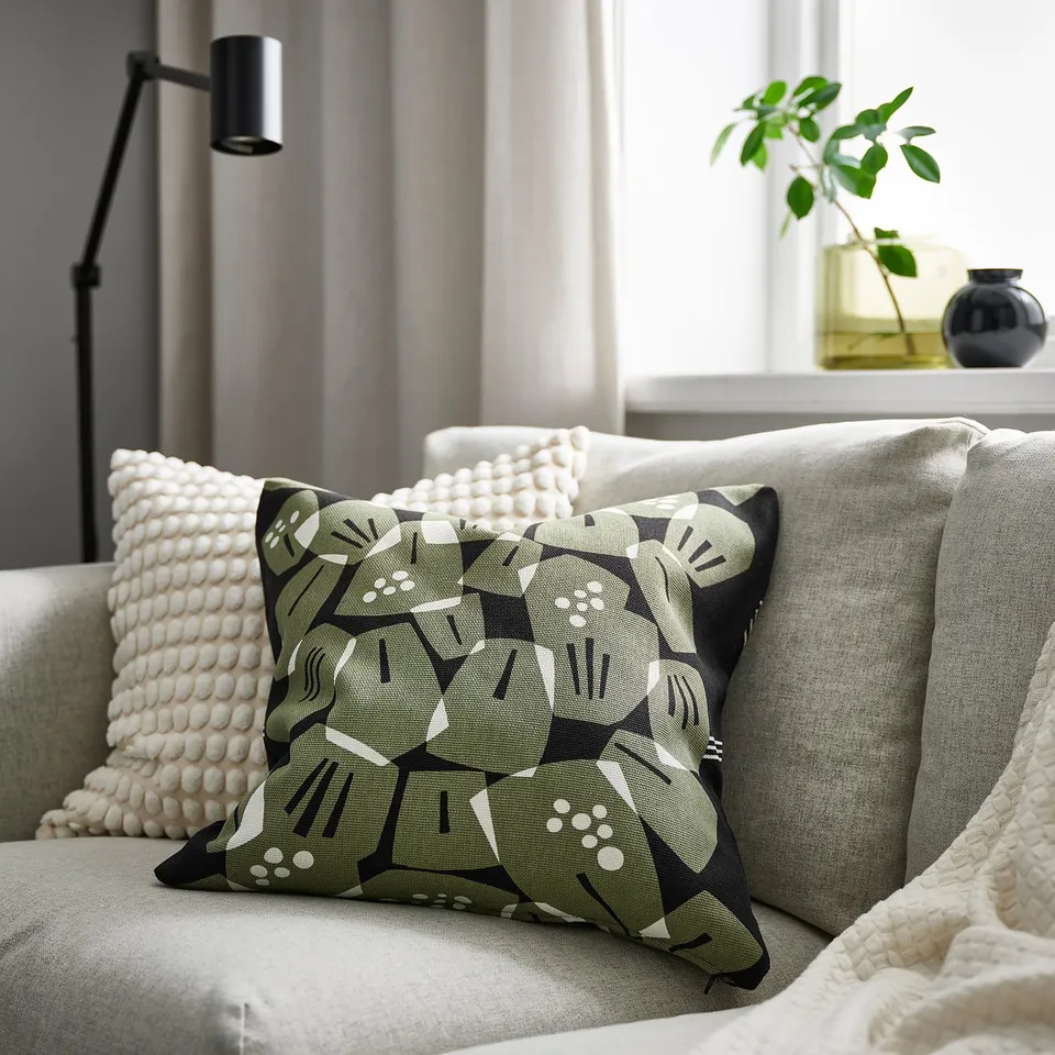 Modern living room with leaf cushion, textured pillows, and blanket on sofa by plant and lamp.