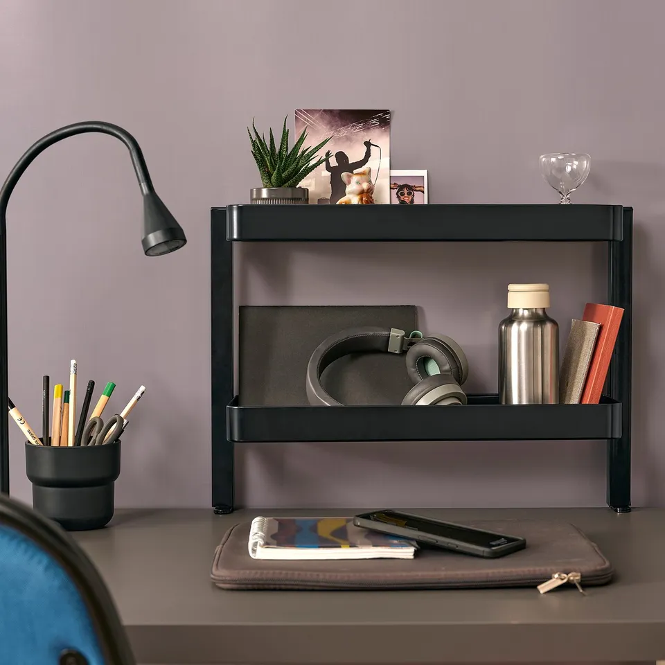 Black VATTENKAR desk shelf, compact, holding various items like headphones, a water bottle, and stationery.