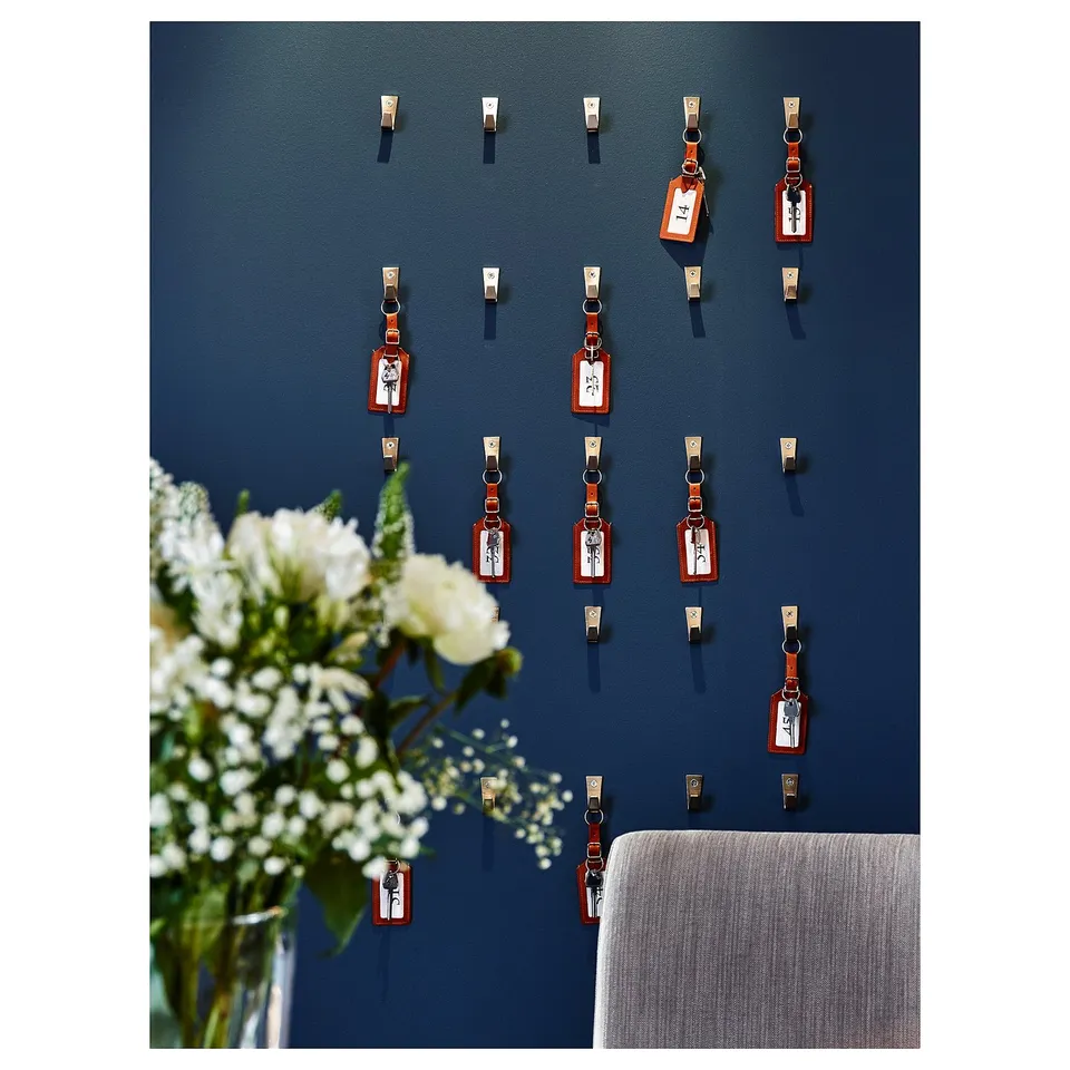 Wall display with multiple blue towel hooks and red tags. White flowers in vase.