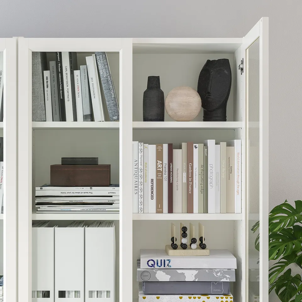 White bookshelf with adjustable, glass doors. It holds various books and decorative items.