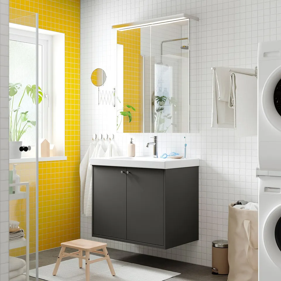 Modern bathroom with dark grey wall-mounted vanity, ceramic sink, large mirror, and bright yellow tiles. Includes storage and a small wooden stool.
