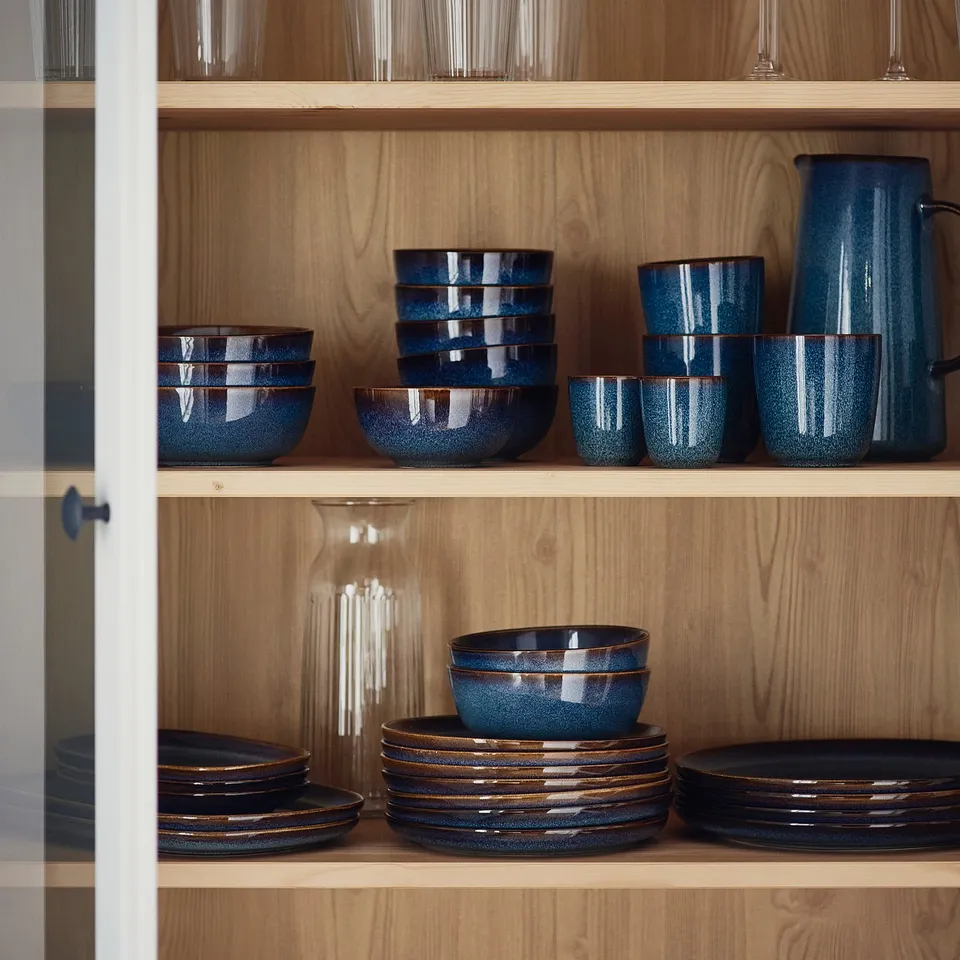 Ocean-blue GLADELIG stoneware jug with golden-brown accents, wider than cups, placed in wooden shelves.