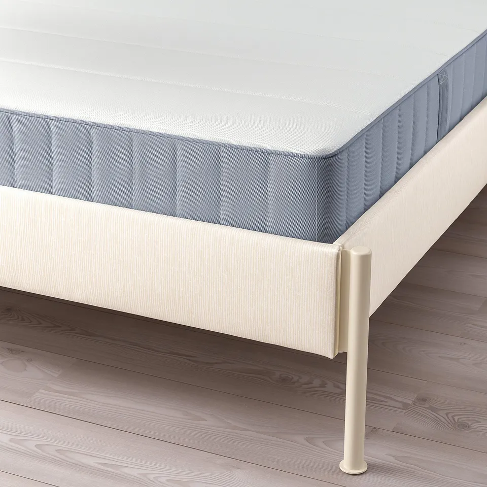 A modern bed frame with light beige, striped upholstery and metal legs, designed for a comfortable mattress.