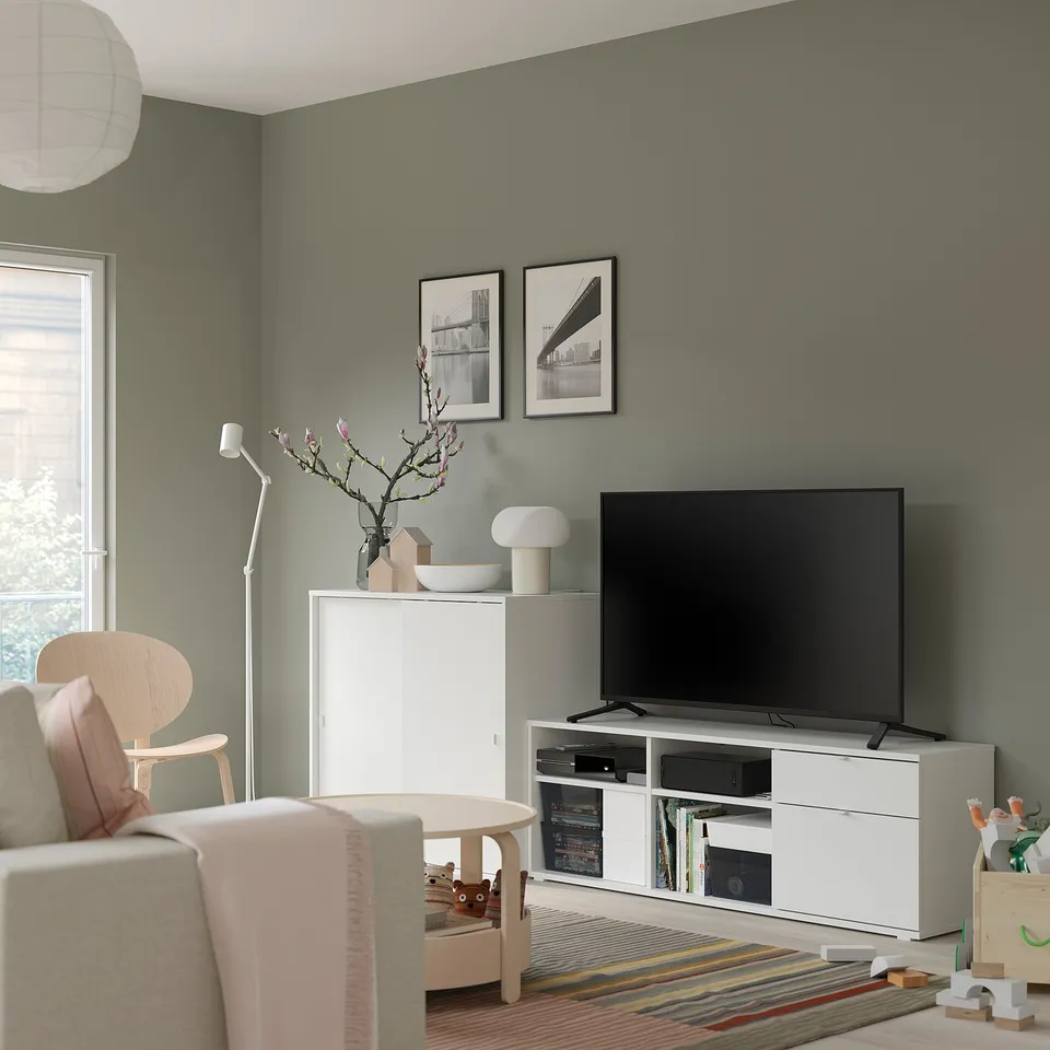 Modern living room with white tv stand, beige chair, colourful rug, and green walls.