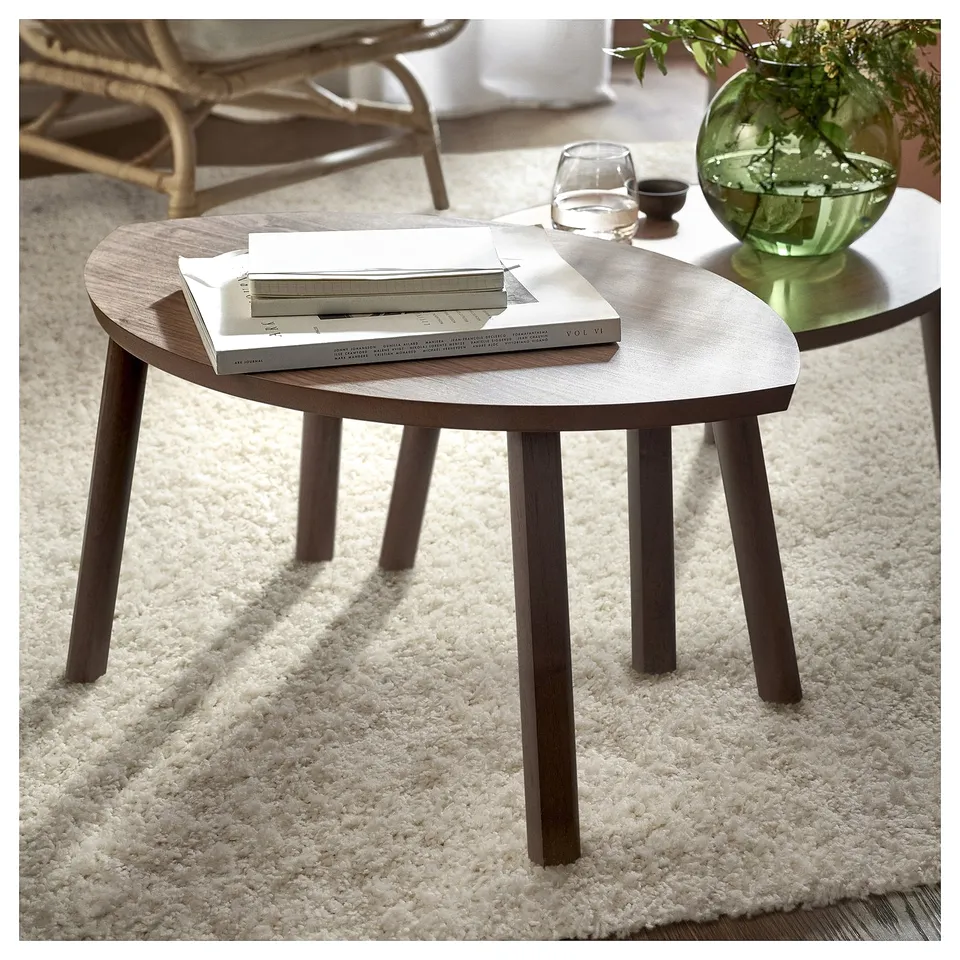 Plush white rug with modern round wooden tables, one holding books, another with a green vase.