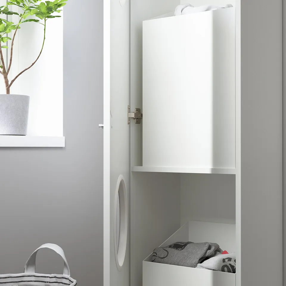 White wardrobe with open lower compartment filled with folded laundry, closed upper door, and potted plant on top.