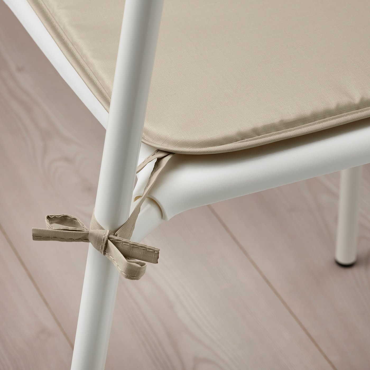 A beige chair pad with ties securing it to a white metal chair leg, showcasing its functionality of staying in place.