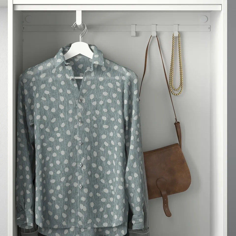 Hanging grey polka-dot shirt with white hanger in closet, leather bag, and gold necklace on hooks.