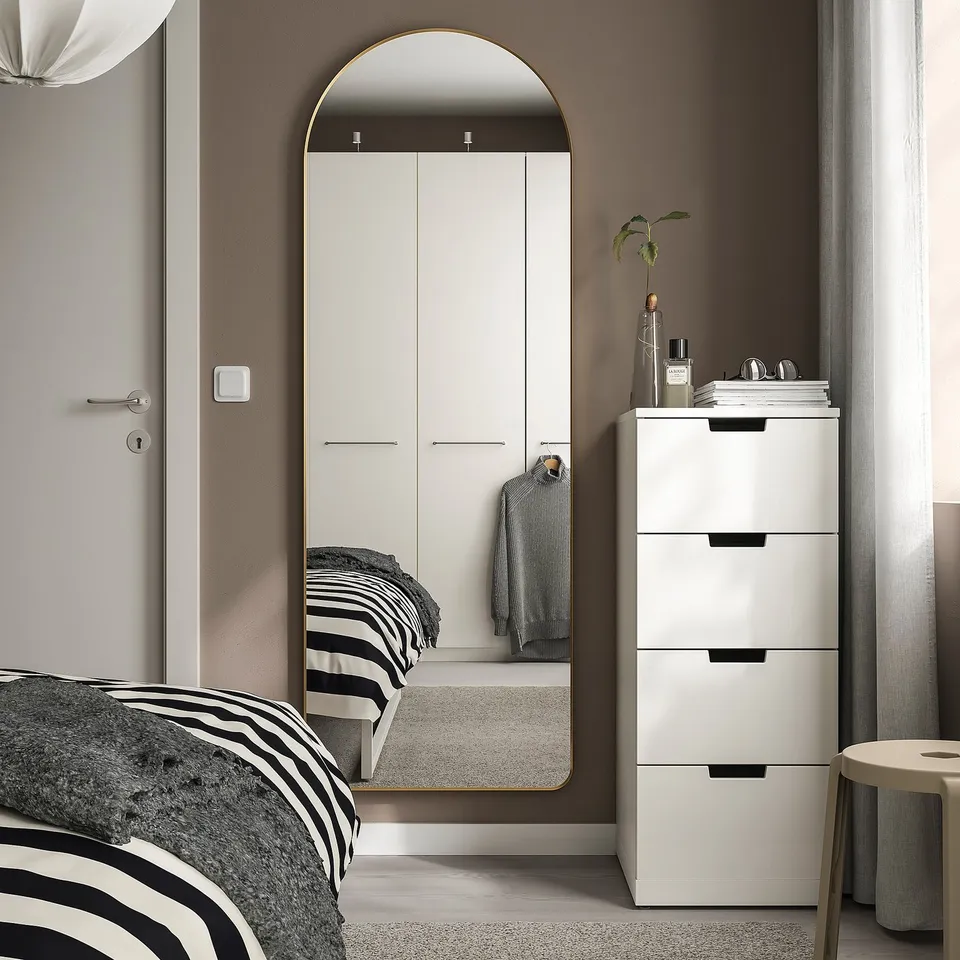 LINDBYN mirror with gold frame against wall next to wardrobe, enhancing room depth.