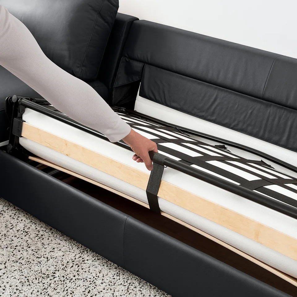 Person pulling out sofa-bed mechanism from black VIMLE sofa.