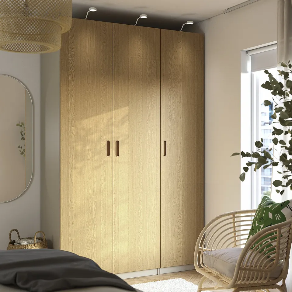 Light oak PAX wardrobe fits between window and wall. Left: mirror, right: wicker chair and plant.