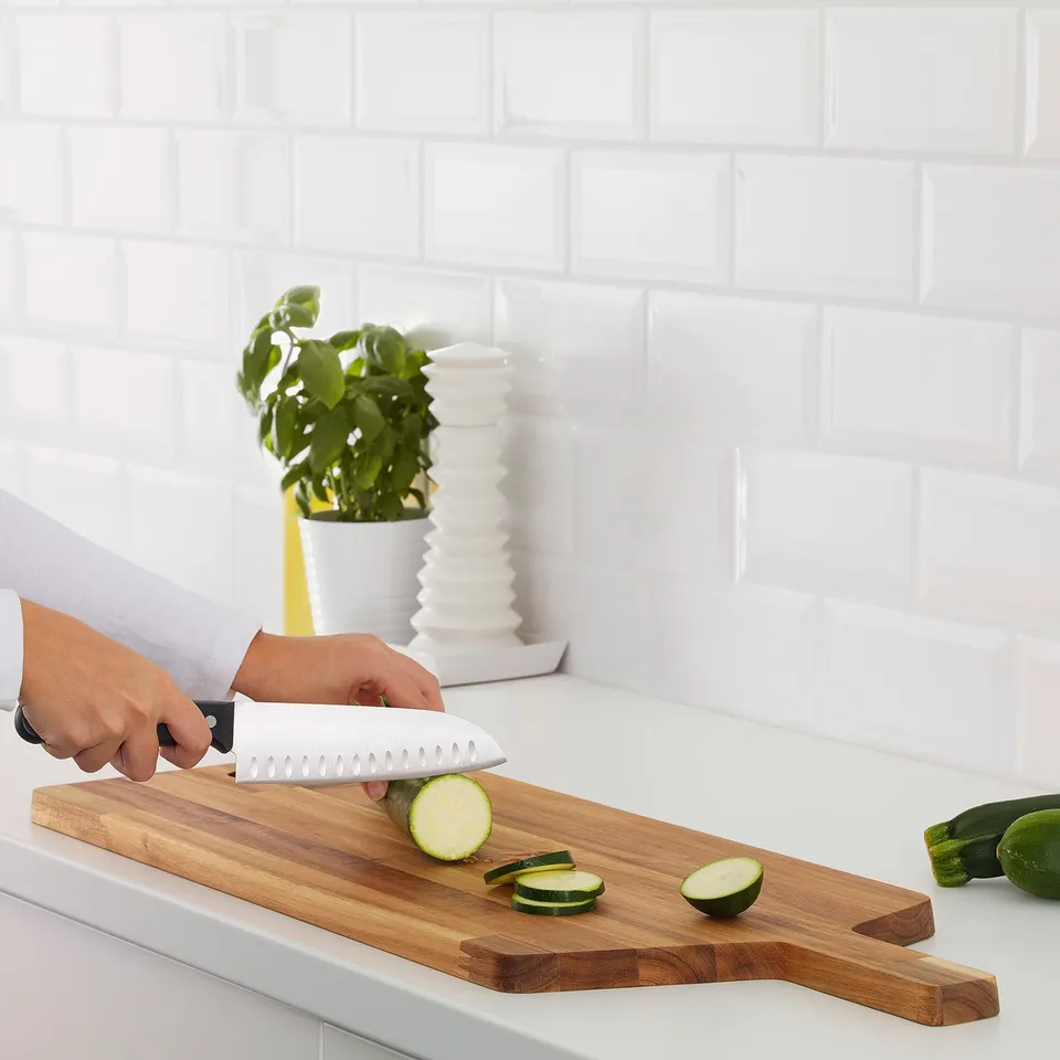 Person slicing courgette on a wooden cutting board.