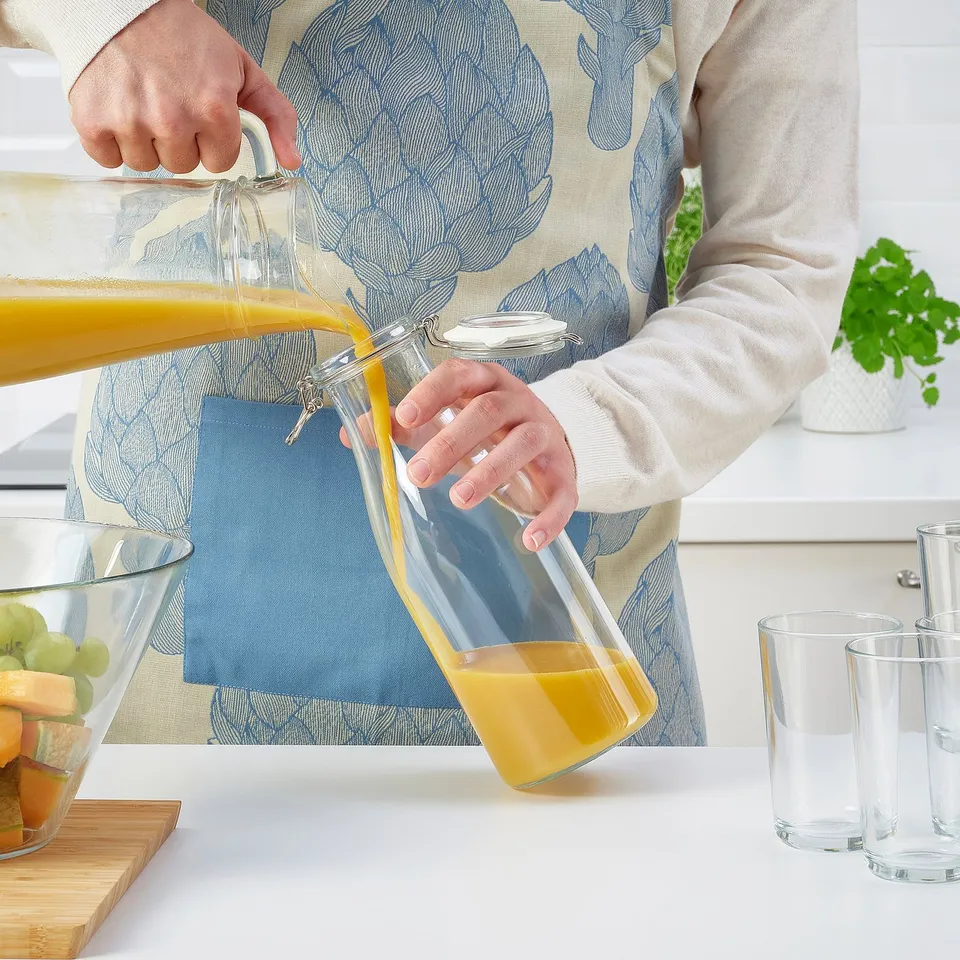 Pouring juice from KORKEN jar; fresh seal, fruits on counter.