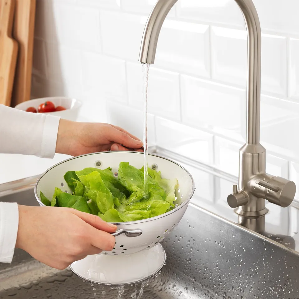 Hands washing lettuce in colander under tap.