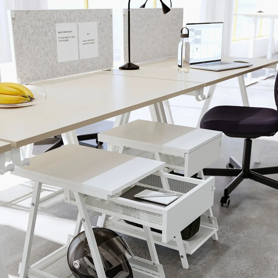 A TROTTEN white metal storage unit with a mesh design, featuring a lockable drawer and an open shelf for a helmet, perfect for desk or living spaces.