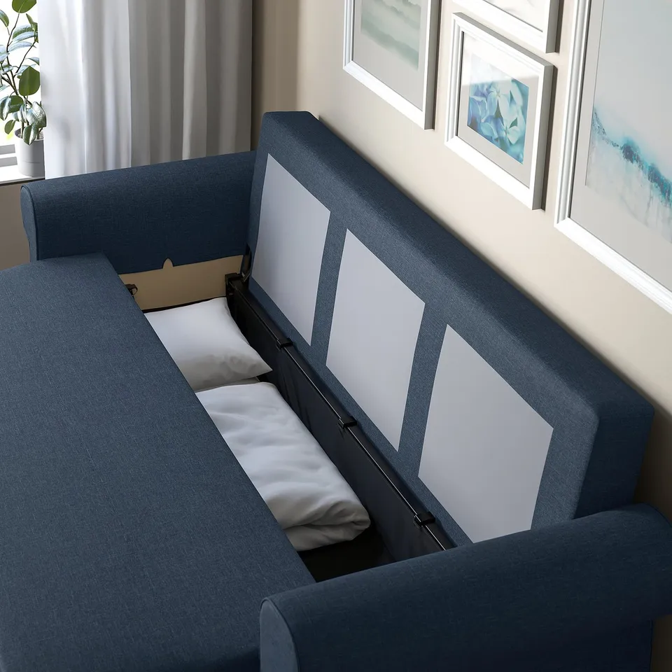 Blue sofa-bed with open storage compartment, pillows inside, under framed, white walls with framed art.