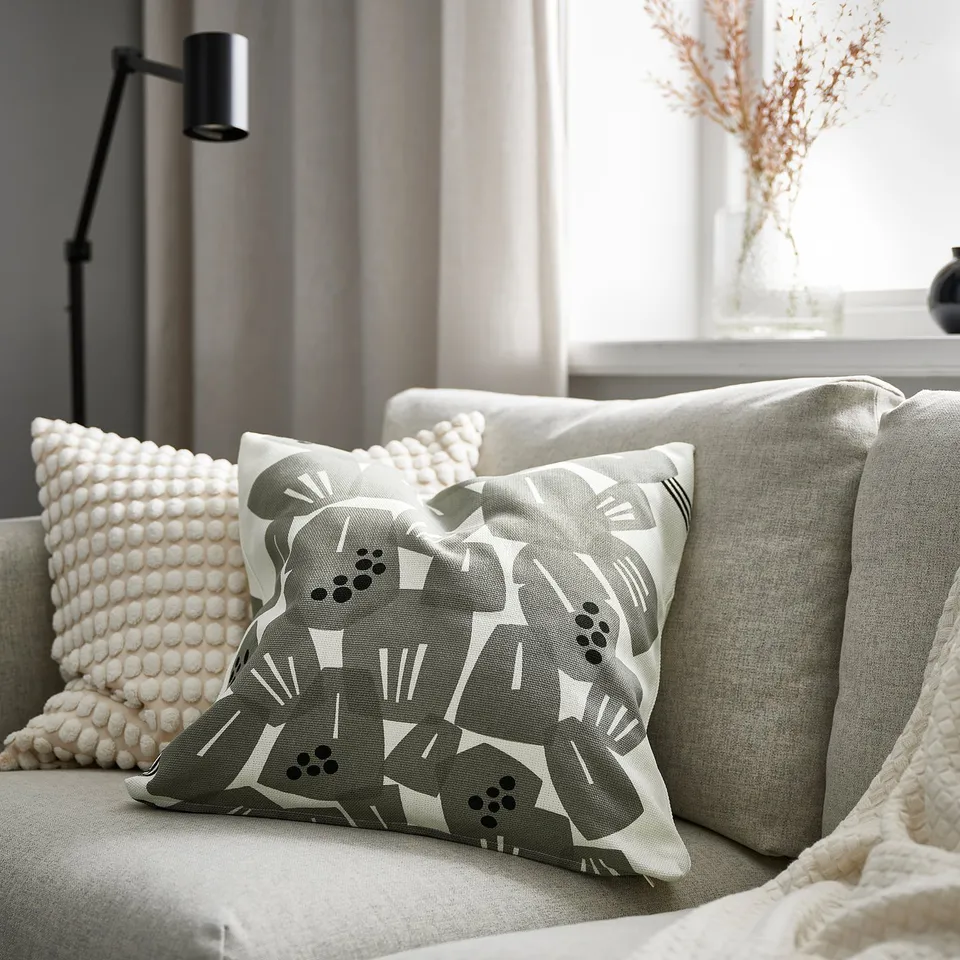 Grey-green underbloppa cushion with leaf pattern on grey sofa, with black lamp & flowers.