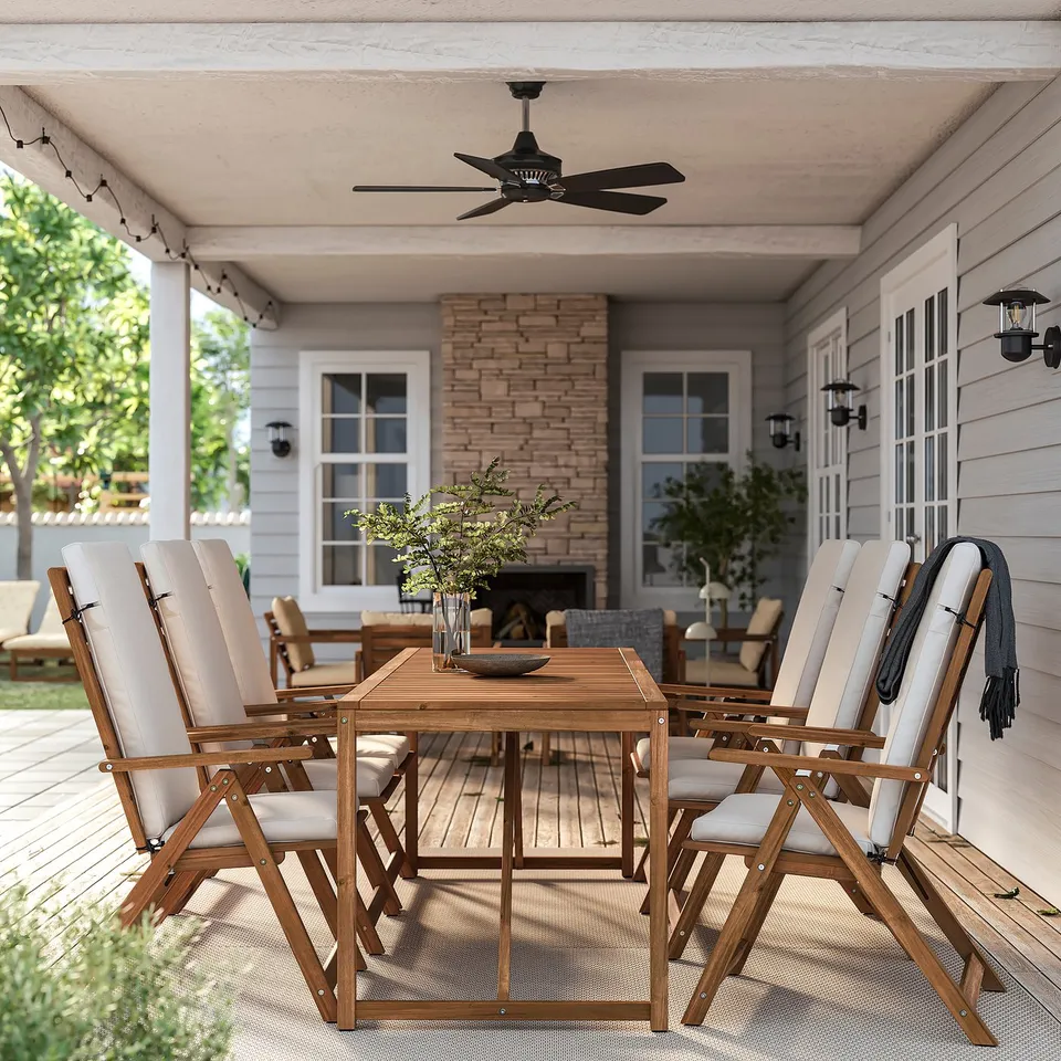 Outdoor dining set with large wooden table and beige chairs. Ceiling fan above, grey house backdrop. Modern, natural design.