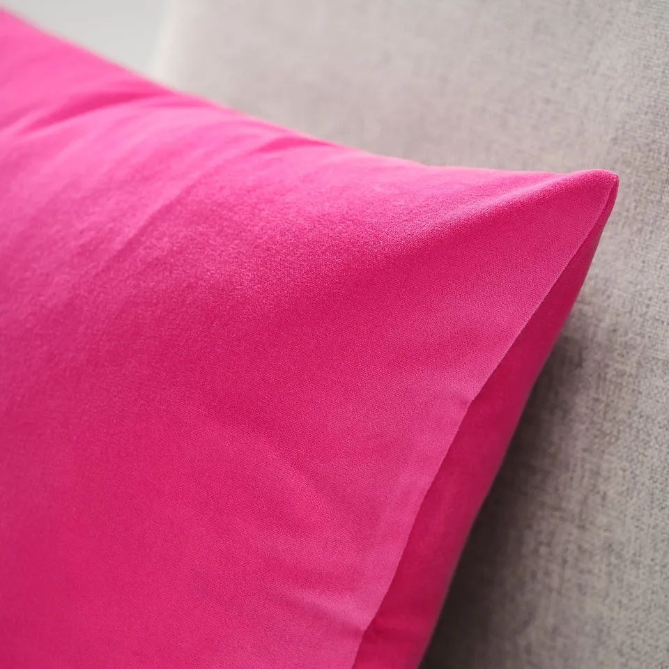 A close-up of a bright pink velvet cushion cover, showcasing its smooth, luxurious fabric and subtle sheen.