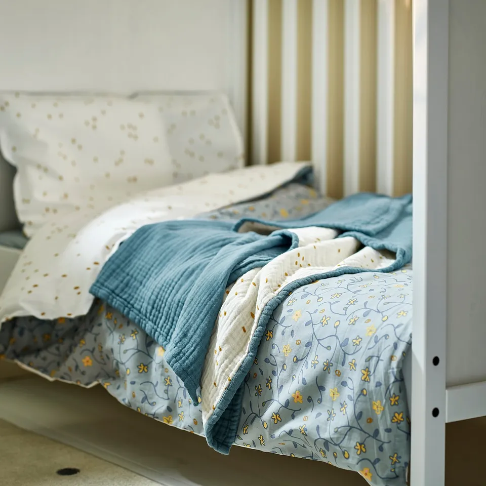Blue & white organic cotton baby blanket with floral pattern on bed.