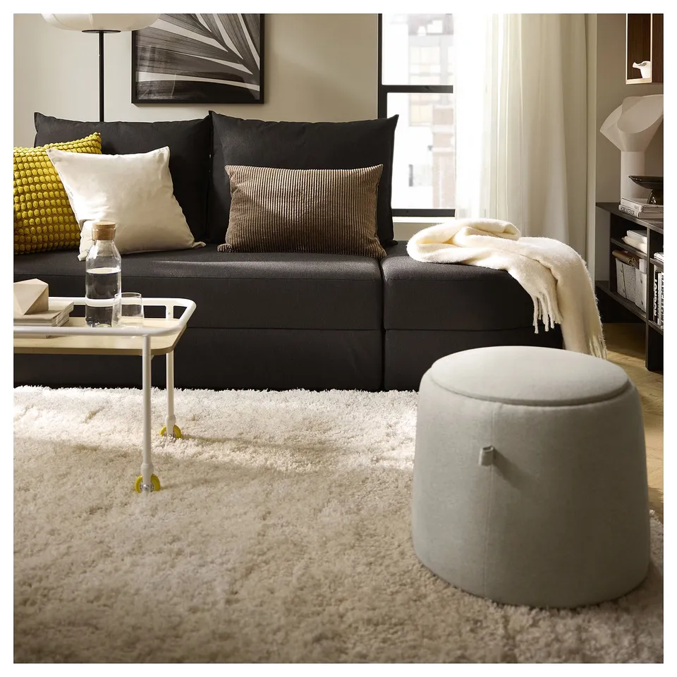 Modern living room with grey sofa, colourful pillows, rug, ottoman, & artwork.