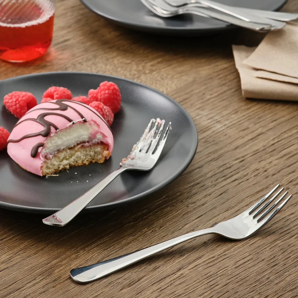 Pink dessert with raspberries on black plate, two forks on wooden table.