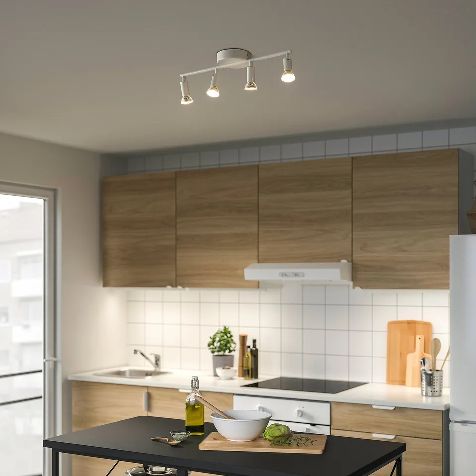Modern kitchen with ceiling lights, wooden cabinets, steel appliances, black island with bowl, cutting board, and olive oil.
