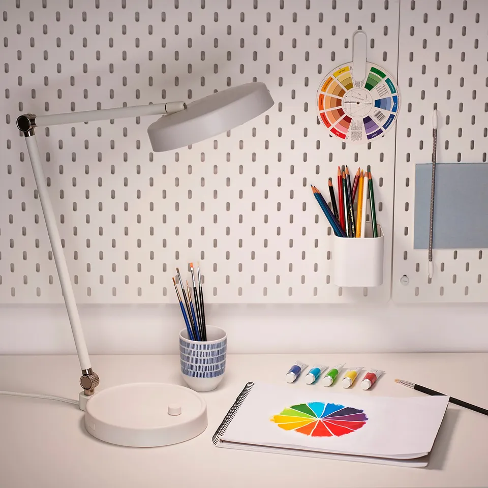 Art desk with lamp, pencils, paints, sketchbook. Pegboard holds colour wheel and supplies. Cosy, creative setup.