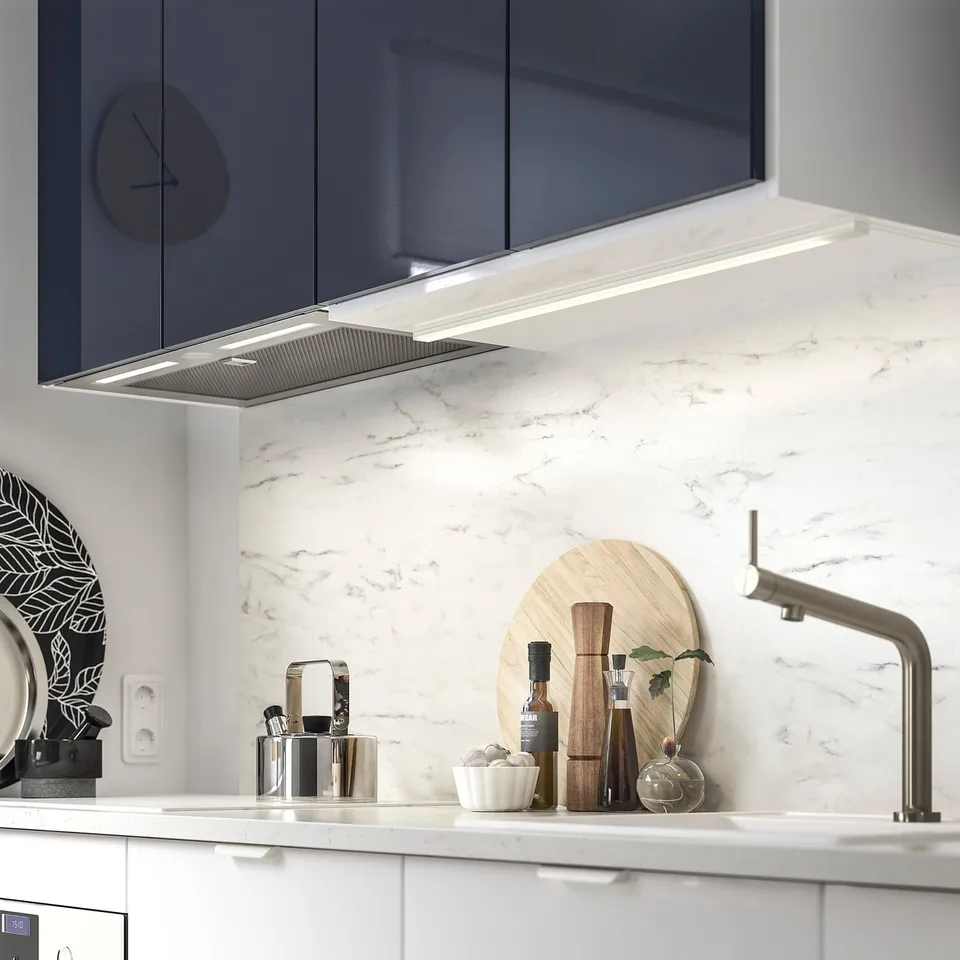 Modern kitchen with sleek white cabinets, built-in range hood, marble backsplash, stainless steel sink, and stylish accessories.