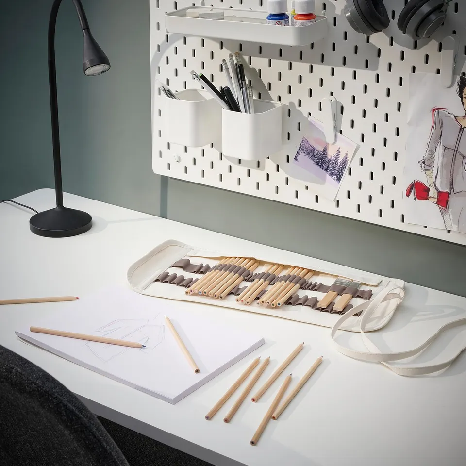 White desk setup with SOLFÅGEL palette, vibrant pencils, organised containers, lamp, sketches, headphones on wall, and drawing tools.