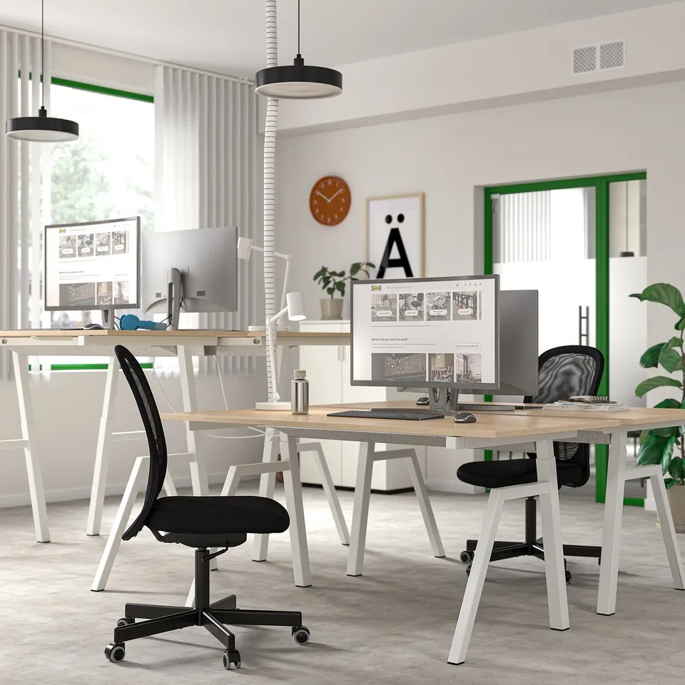 Office with TROTTEN sit-stand desks, chairs, and monitors. Room is well-lit and decorated.