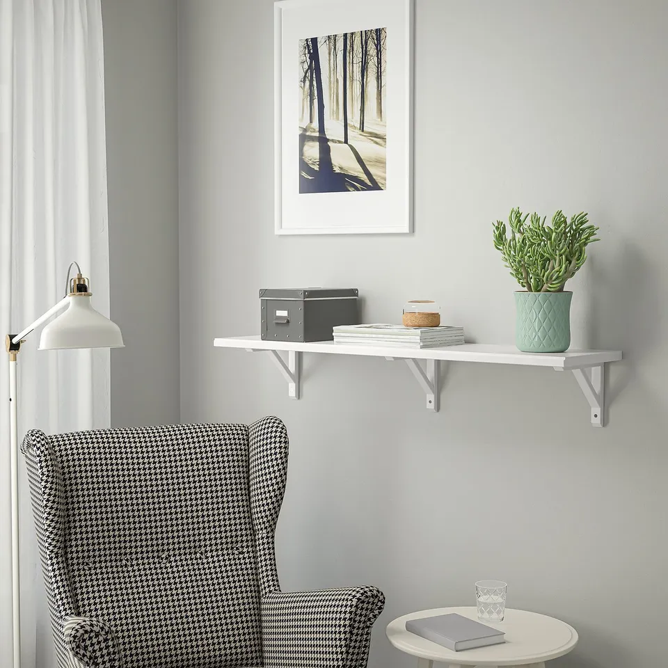 Wall shelf with plant & books above houndstooth chair & side table lamp.