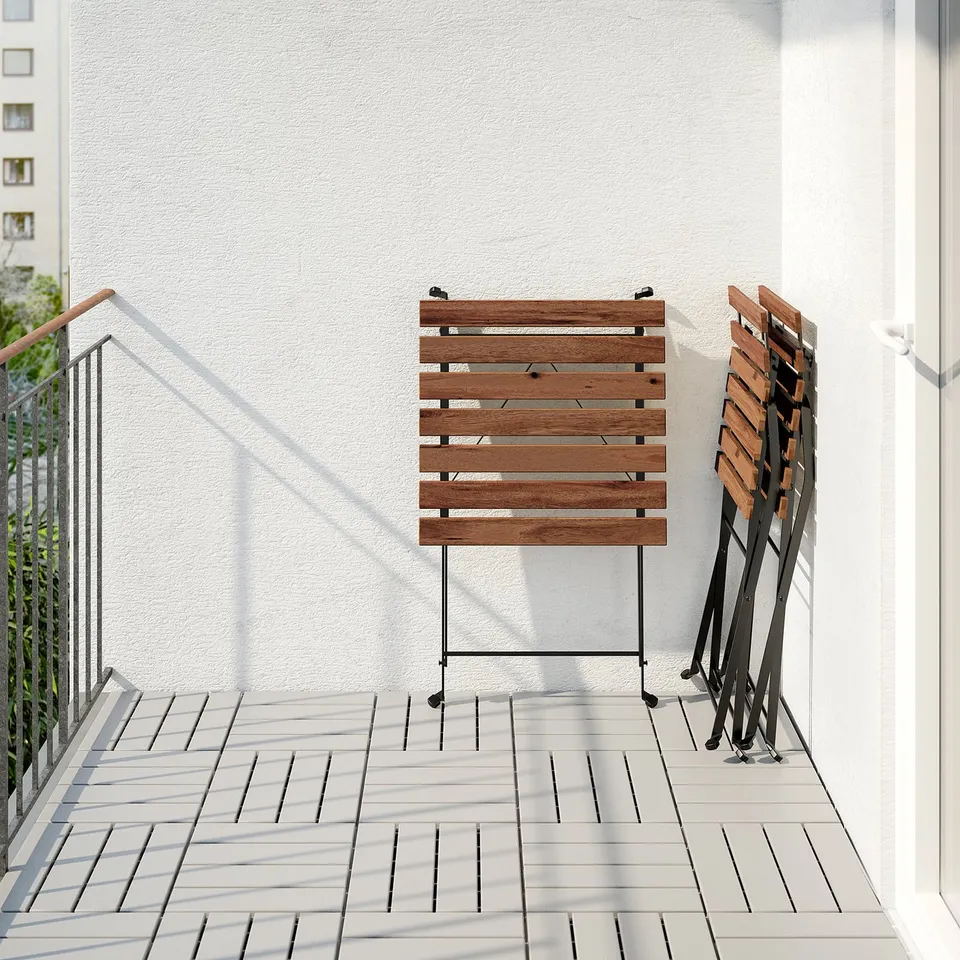 Balcony with wooden table and folded chairs neatly stacked against white wall.
