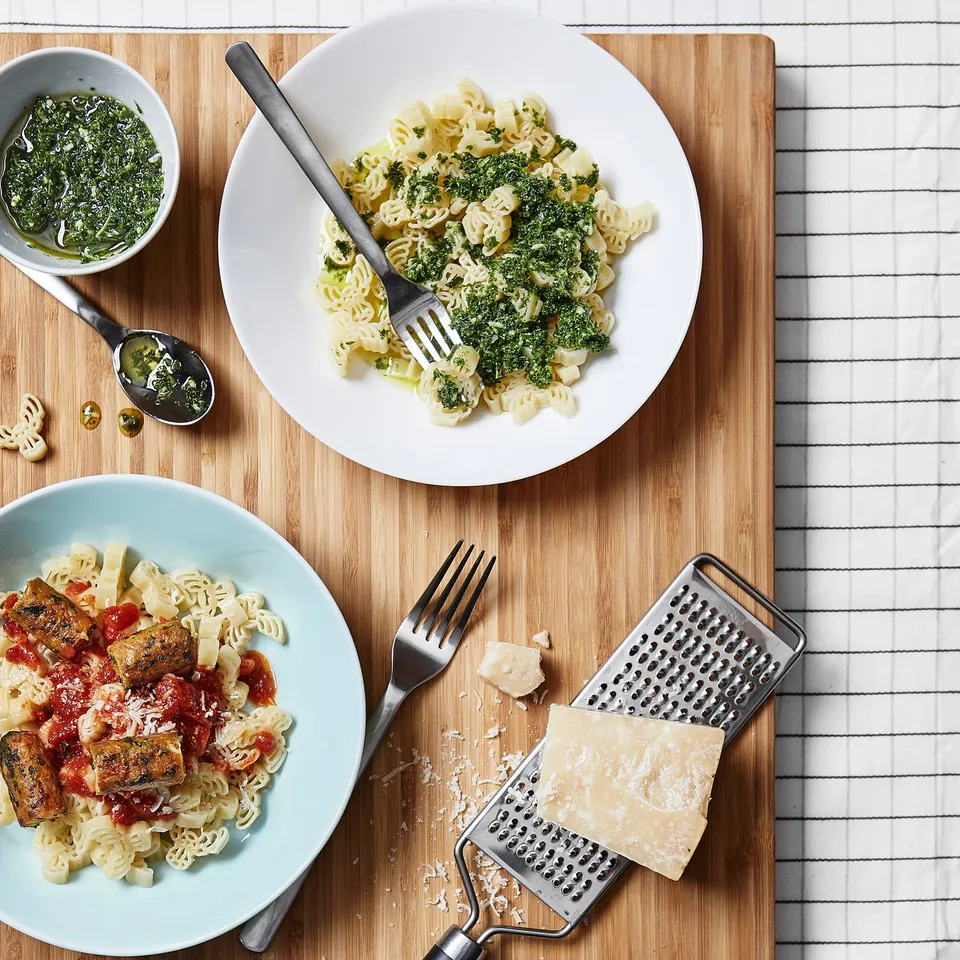 Two pasta dishes: green, tomato sauces. Forks, grater. Elk-shaped pasta.