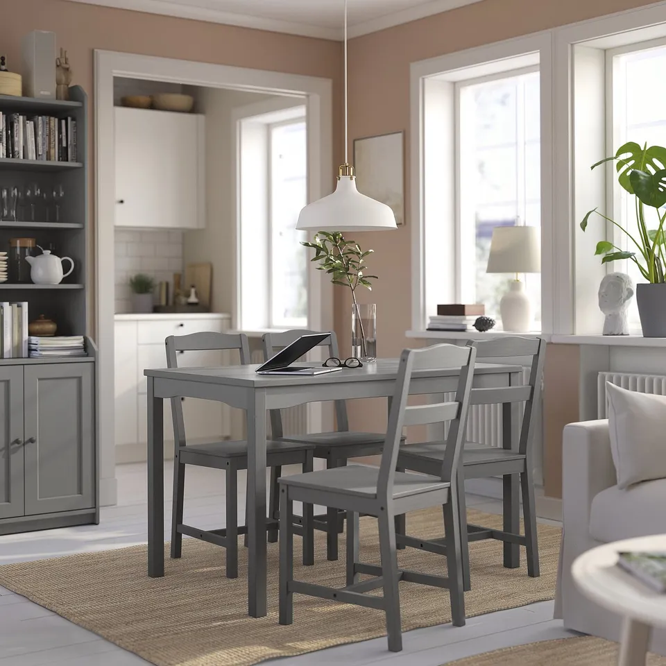 Modern grey dining set in living room with wooden table and four matching chairs. White pendant light, natural decor, and large windows.