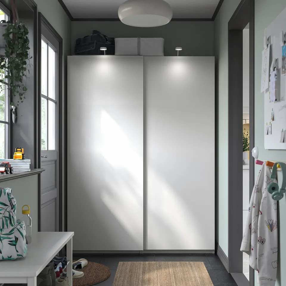Modern closet with sliding doors. White doors, grey walls, built-in lighting, and a rug.