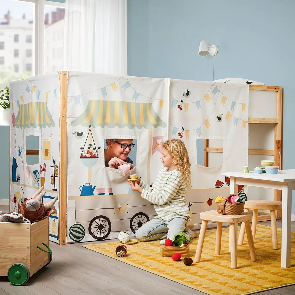 In a bright playroom, a child plays tea party with a toy set, using cups and saucers on a small table.