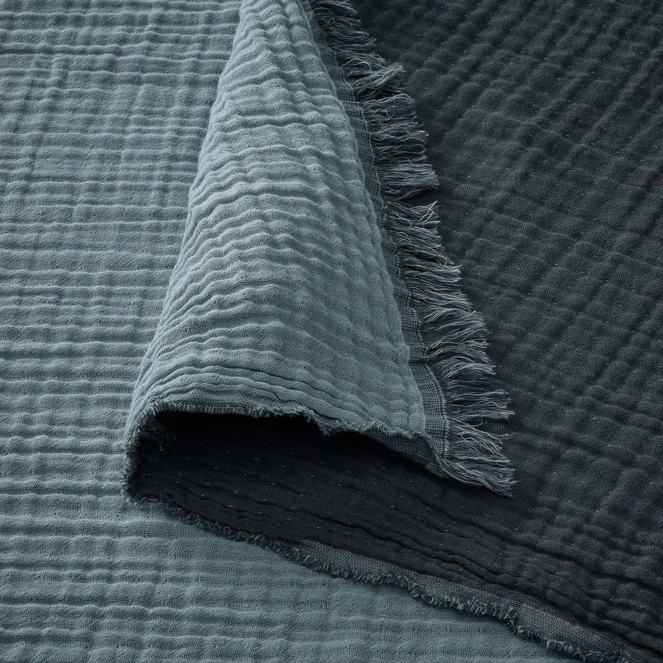 Soft, crinkled fabric with raw edges, likely made of cotton, draped over a dark surface. Textured, natural fibres showcase a woven design.