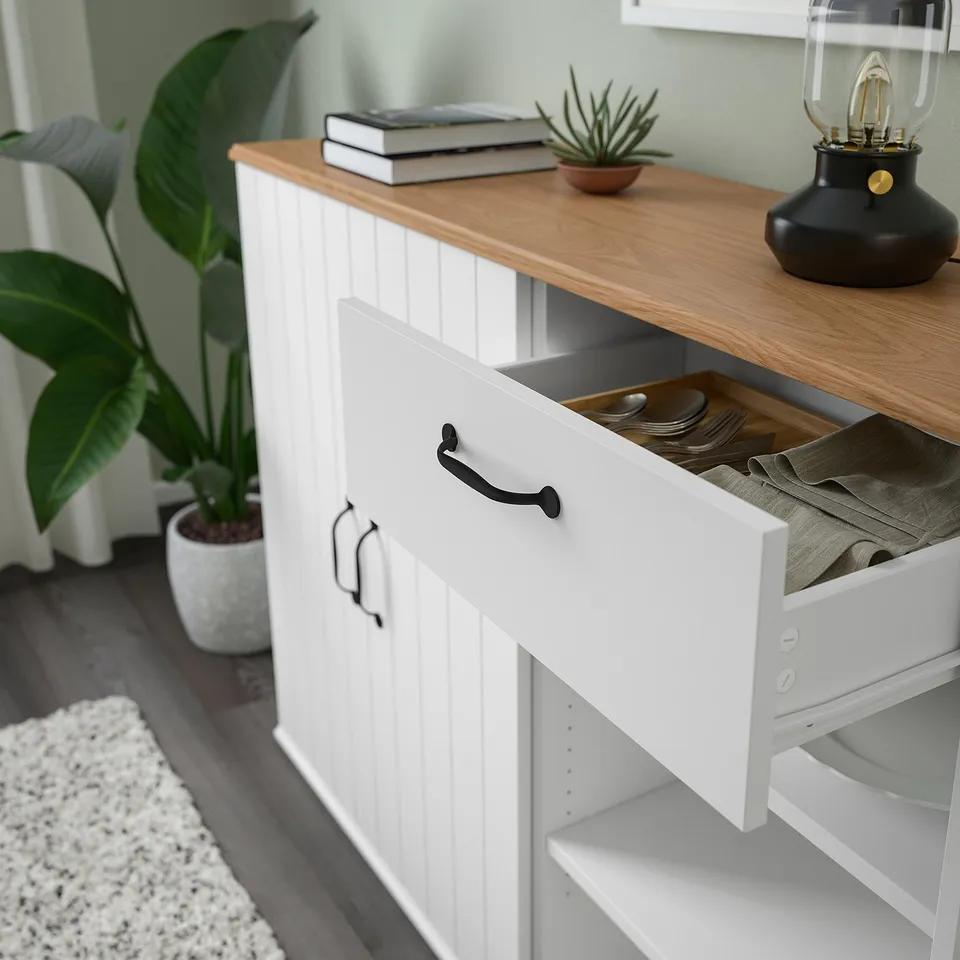 White cabinet with open drawer revealing napkins, wooden top with books and plant.