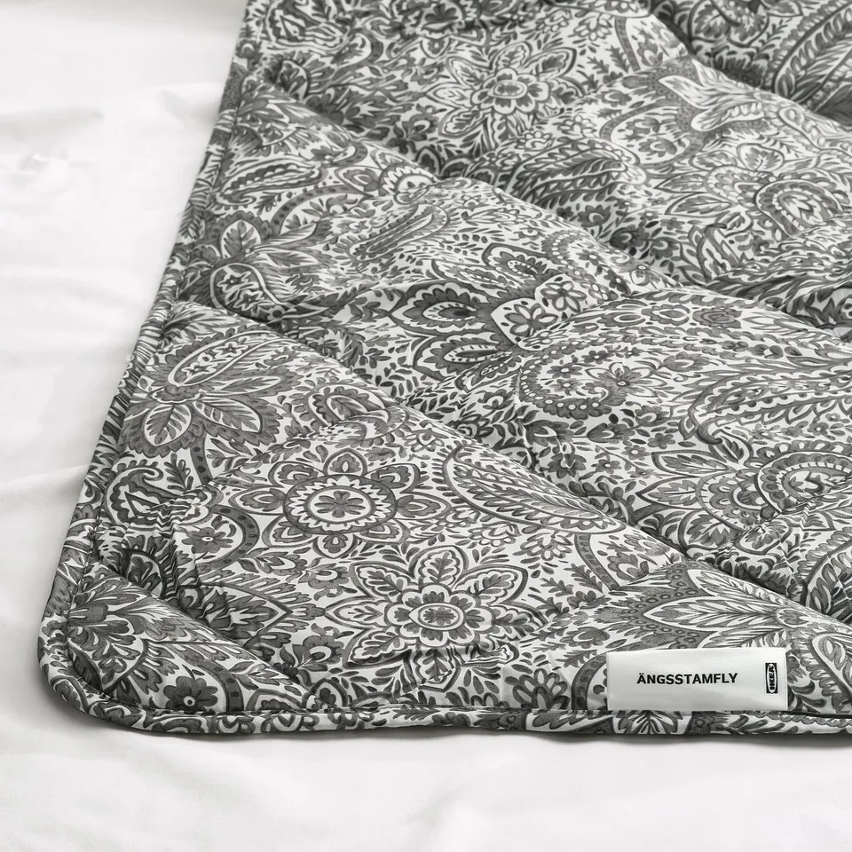 Intricate grey and white patterned duvet, neatly folded; label reads ÄNGSSTAMFLY.