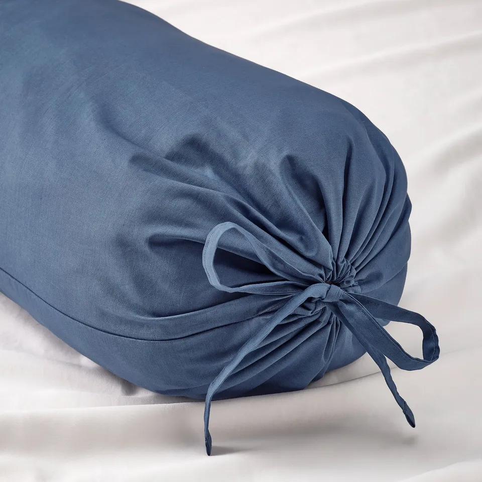 Blue circular bolster pillow with tied fabric ends on white surface.