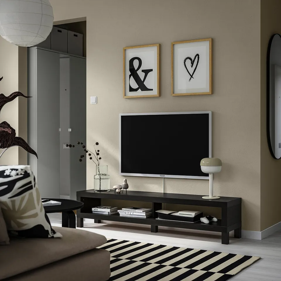 Modern living room with bLACK tv bench, flat-screen tv, gold art, lamp, and striped rug, grey sofa, round table.