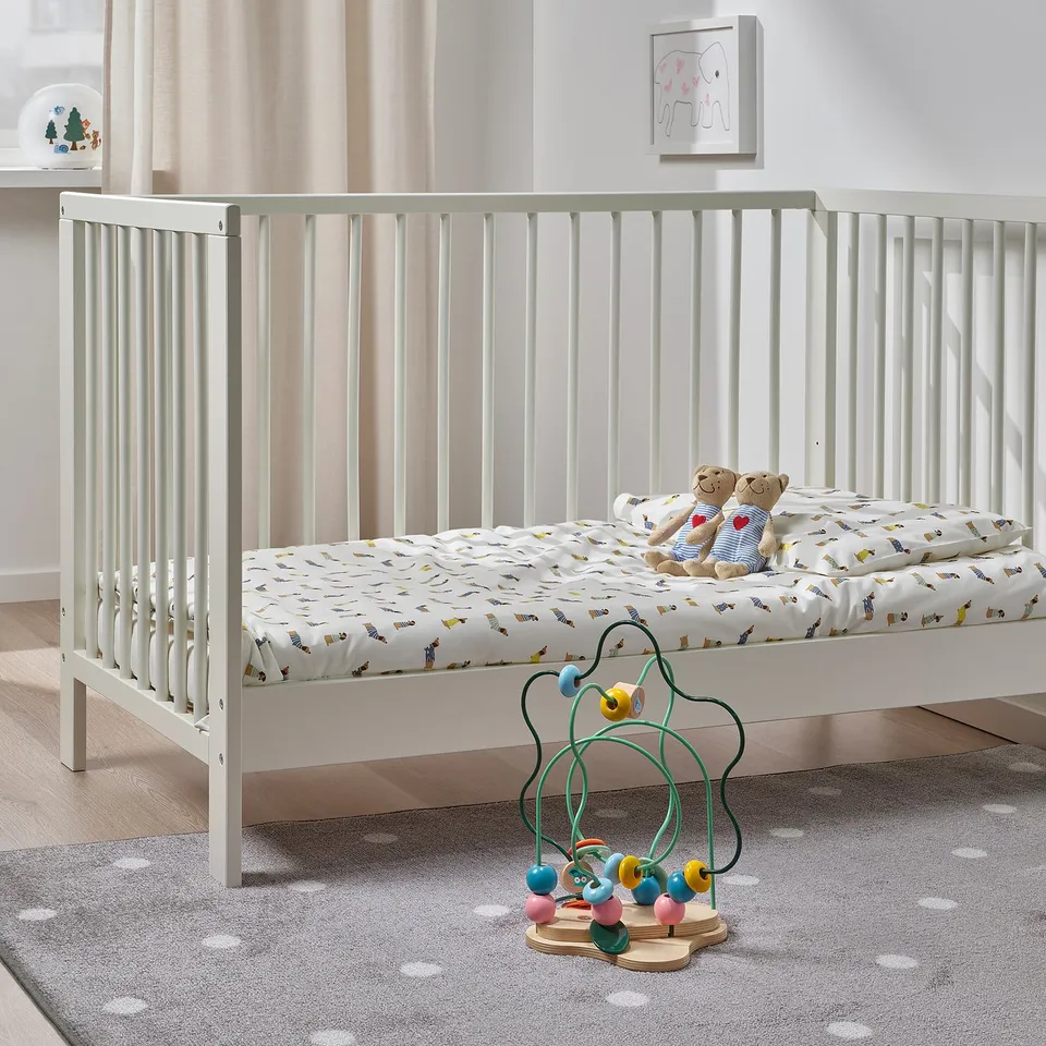 White wooden crib with stuffed animals, baby mobile, and floor toy. Crib is larger than other items.